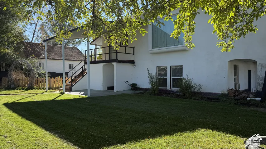 Backyard featuring a paved patio, elevated deck with railing, arched entryway, and mature tree canopy