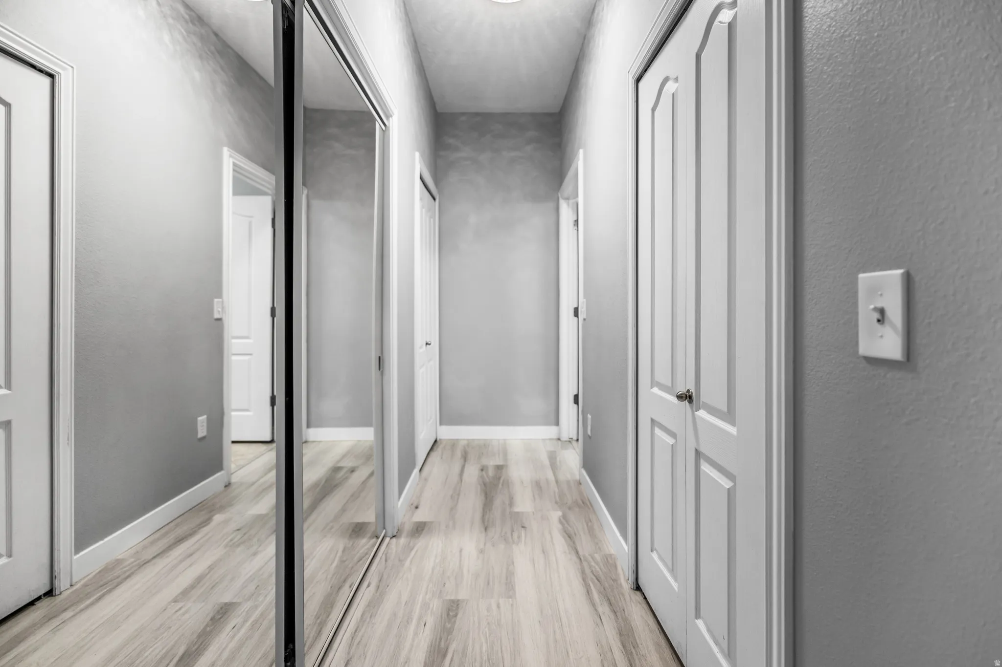 Hallway featuring light wood-finish flooring, light gray walls, white baseboards, and multiple white paneled doors