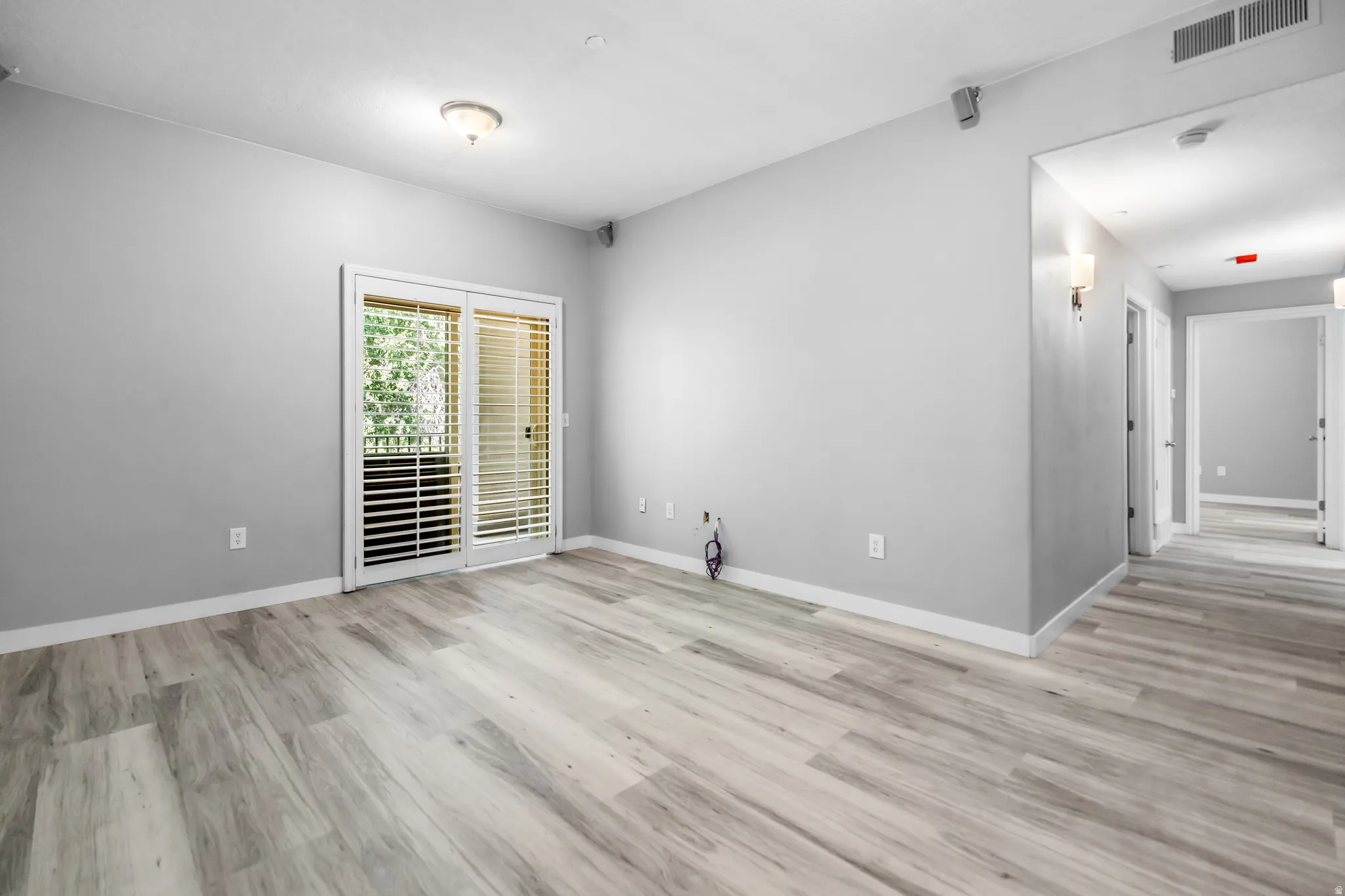 Spacious room featuring wood-finish flooring, light grey wall tones, and white baseboards