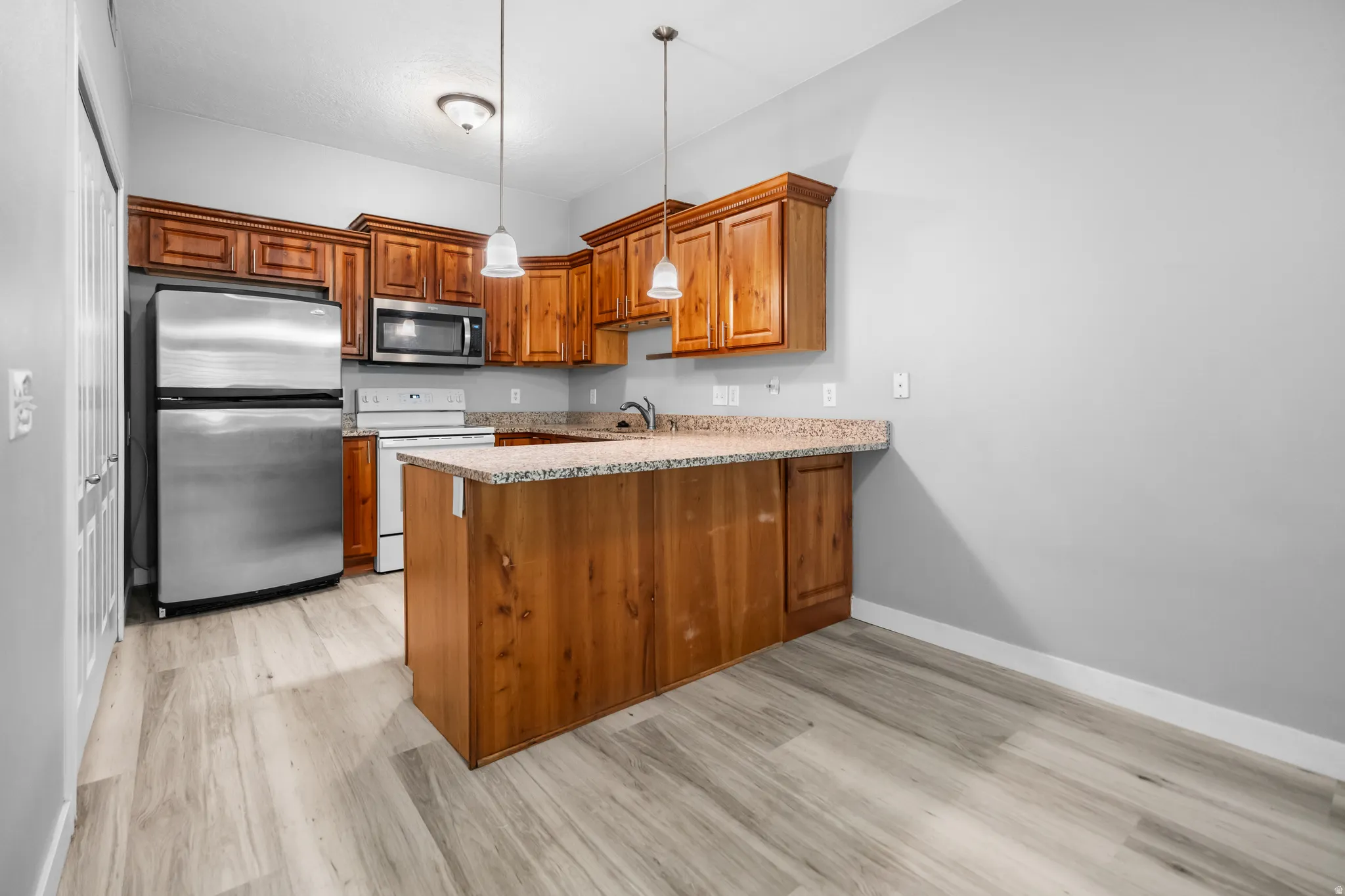 Kitchen featuring wood cabinetry, stainless steel appliances, a center island with a granite-style countertop, and wood-finish flooring