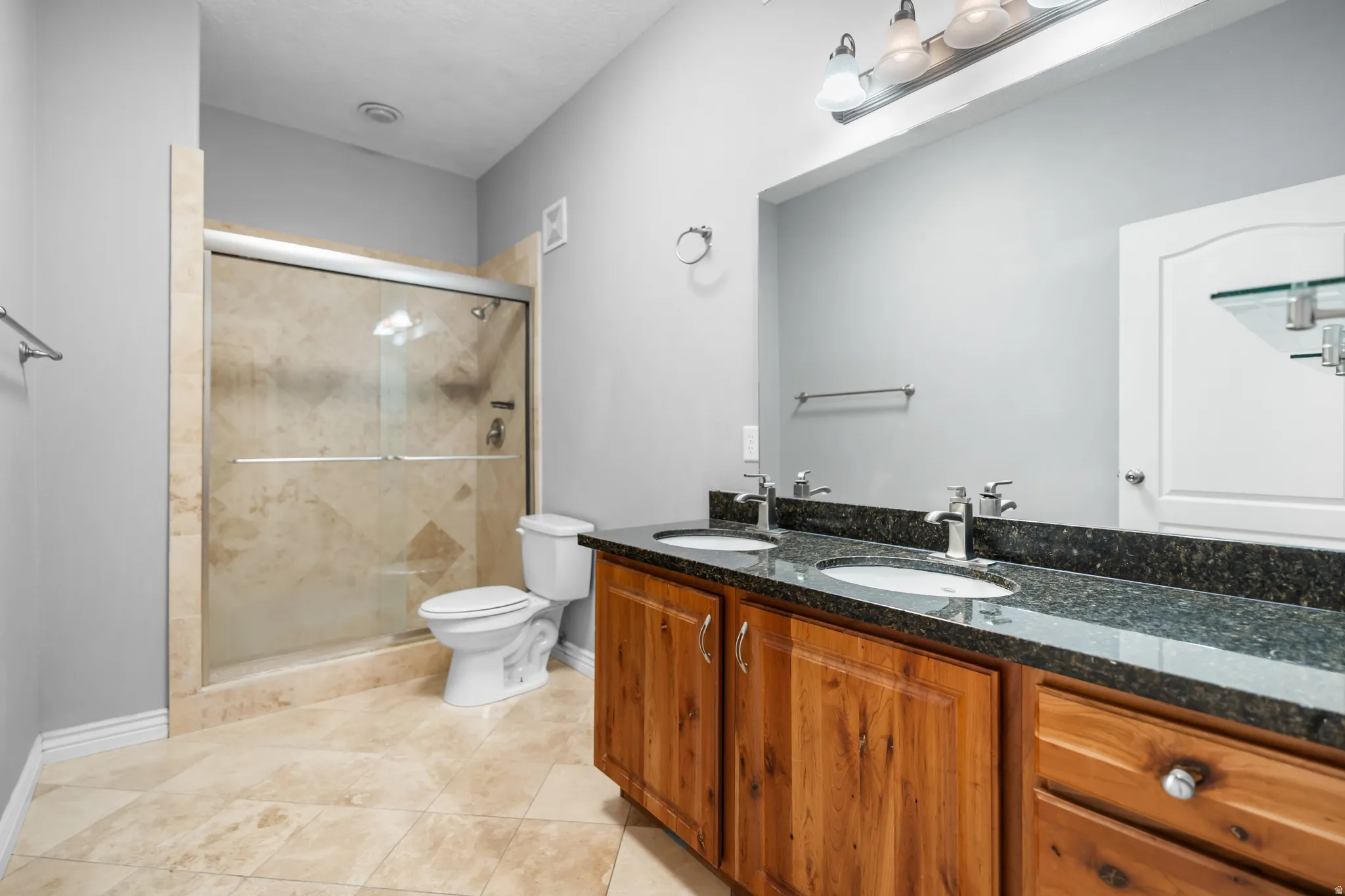 Bathroom featuring a dual vanity with a dark speckled countertop and wood cabinetry