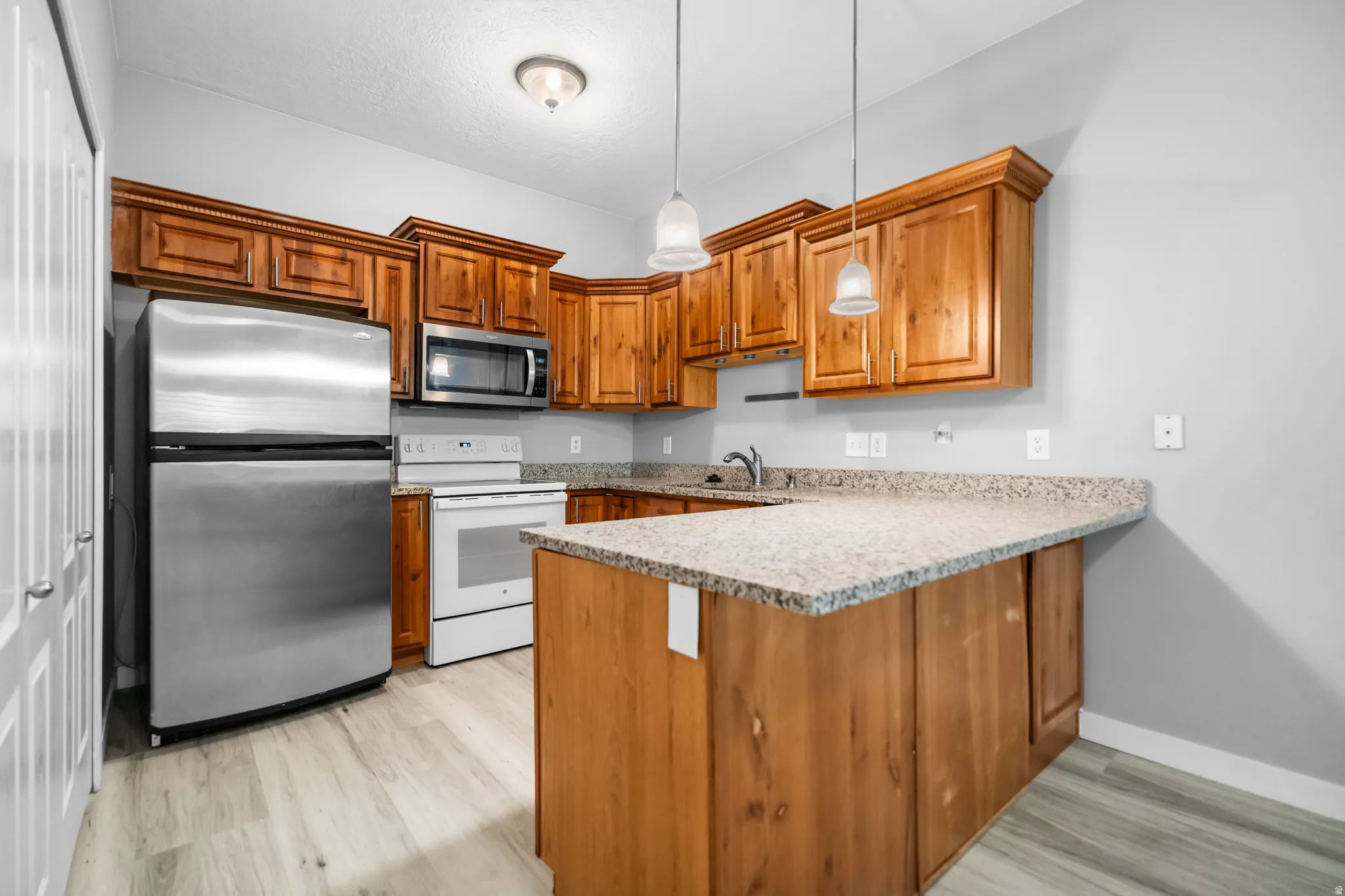 Kitchen with wood-finish cabinetry, light gray walls, light wood-finish flooring, and a stone-finish countertop