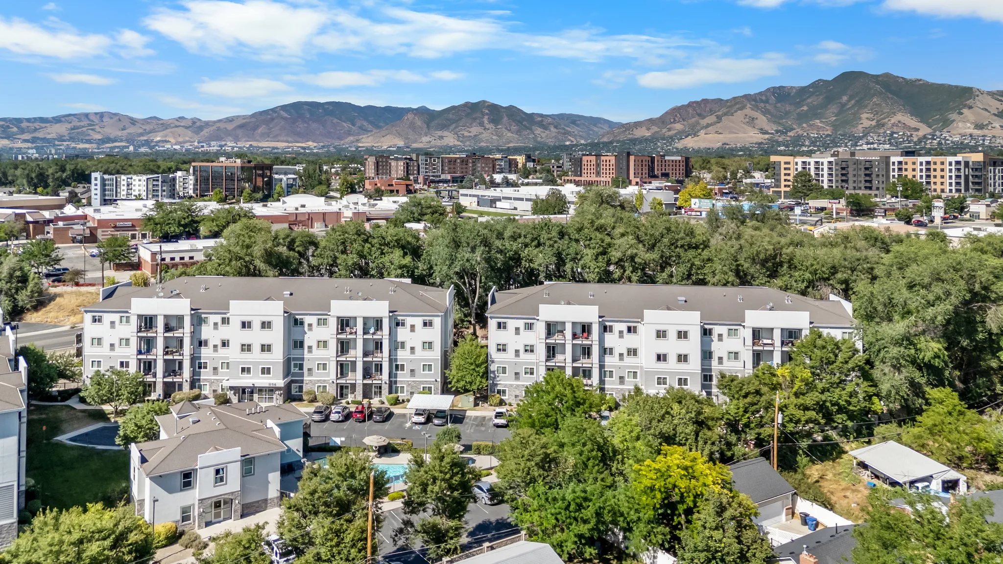 Modern multi-story apartment buildings featuring private balconies and surrounding mature trees
