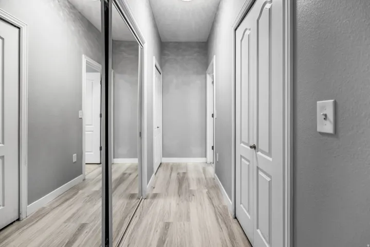 Hallway featuring light wood-finish flooring, light gray walls, white baseboards, and multiple white paneled doors