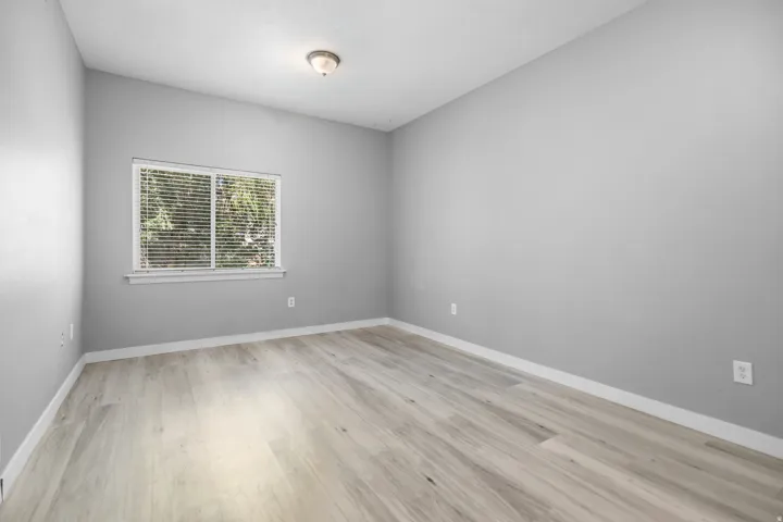 Interior room featuring light gray walls, wood-finish flooring, white baseboards, and a window with white blinds