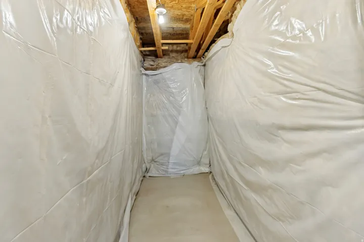 Crawl space with white vapor barrier lining the walls and a concrete floor