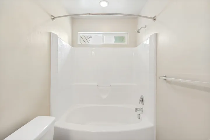 Bathtub and shower combination featuring a curved shower rod, chrome fixtures, and a transom window