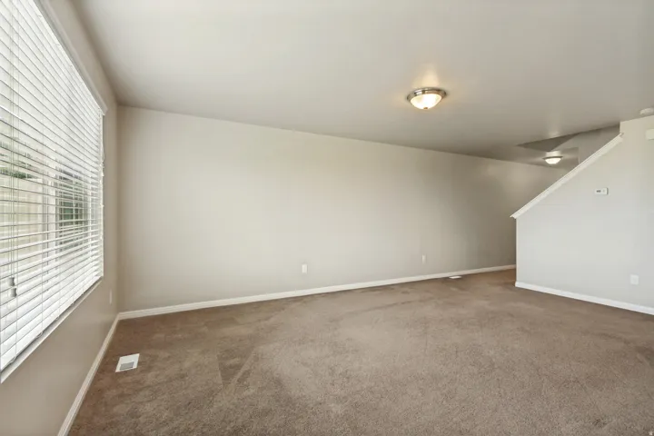 Spacious room featuring neutral carpeting, a large window with horizontal blinds, and warm overhead lighting
