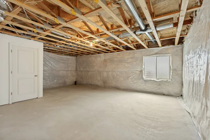 Unfinished basement featuring exposed wood ceiling joists, concrete flooring, and a single egress window