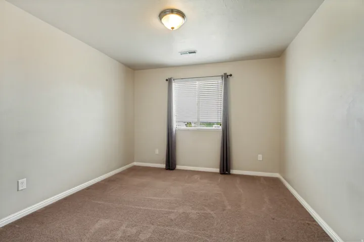 Carpeted room featuring a window with horizontal blinds and drapes, light-toned walls, white baseboards, and a flush-mount ceiling light fixture
