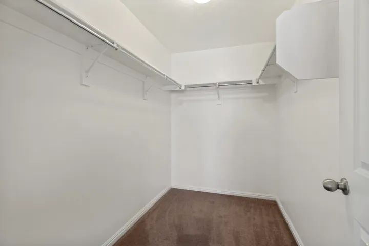 Spacious walk-in closet featuring white wire shelving, hanging rods, and a brown carpeted floor