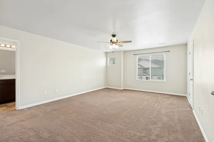 Spacious room featuring neutral carpeting, light-toned walls, and a ceiling fan with integrated lighting