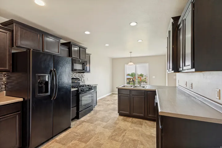 Kitchen featuring dark wood-finish cabinetry, black appliances, mosaic tile backsplash, recessed lighting, and a sliding glass door