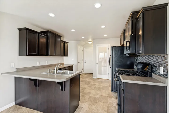 Kitchen featuring dark wood cabinetry, a double basin sink, and black appliances