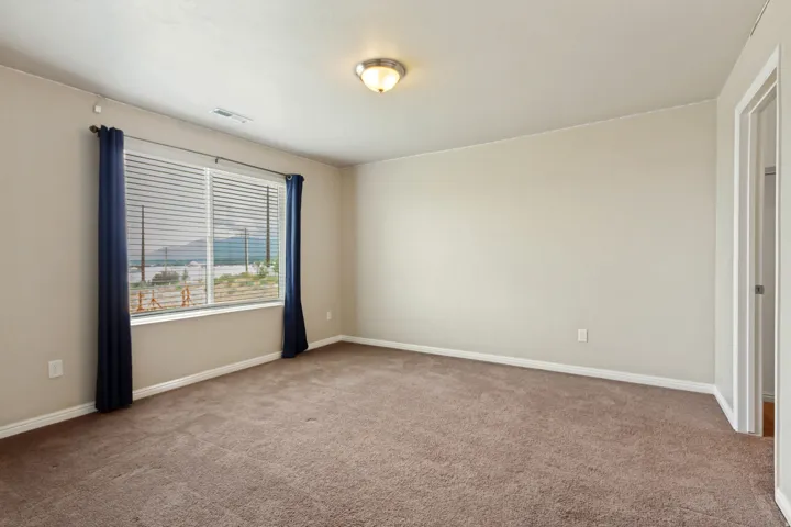 Carpeted room featuring a large window with horizontal blinds, neutral wall paint, and a semi-flush ceiling light fixture