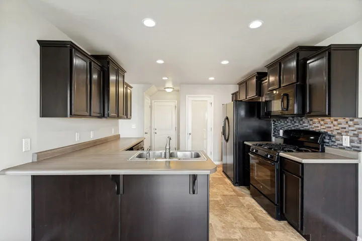 Modern kitchen featuring dark wood-finish cabinetry, stainless steel double basin sink, neutral countertops, and a mosaic tile backsplash