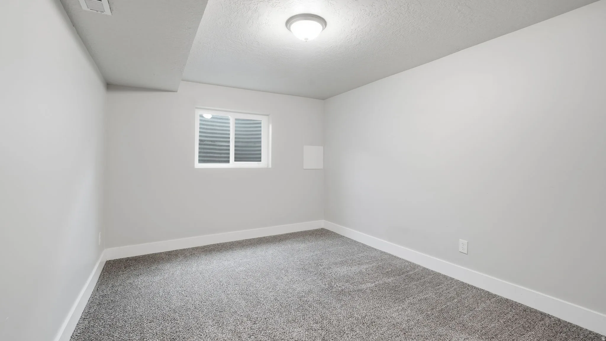 Carpeted bedroom downstairs with closet and window.