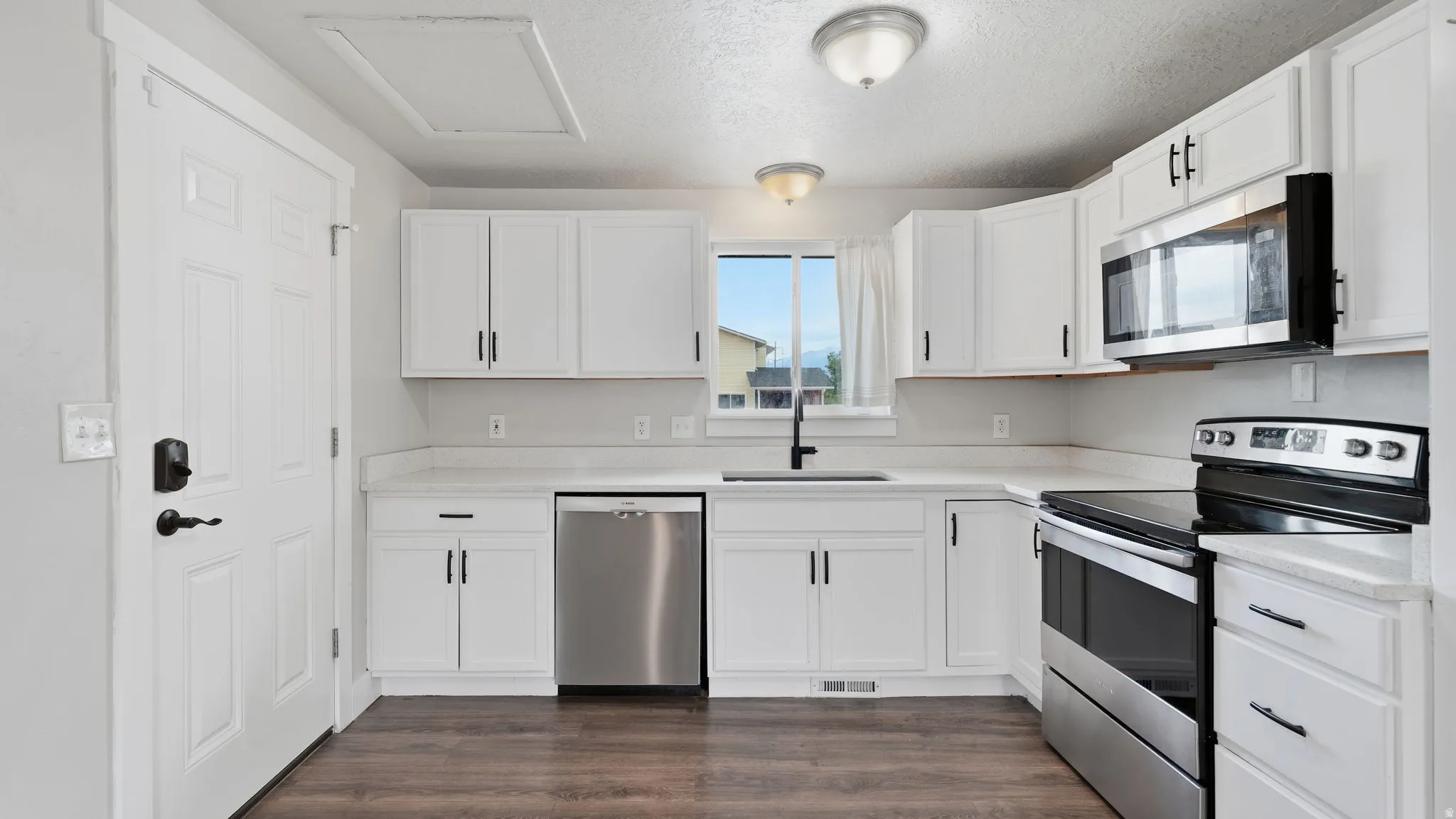 Kitchen with pantry closet featuring quartz countertops, large sink, stainless steel appliances, a view of the Wasatch mountains, and a side door to the yard.