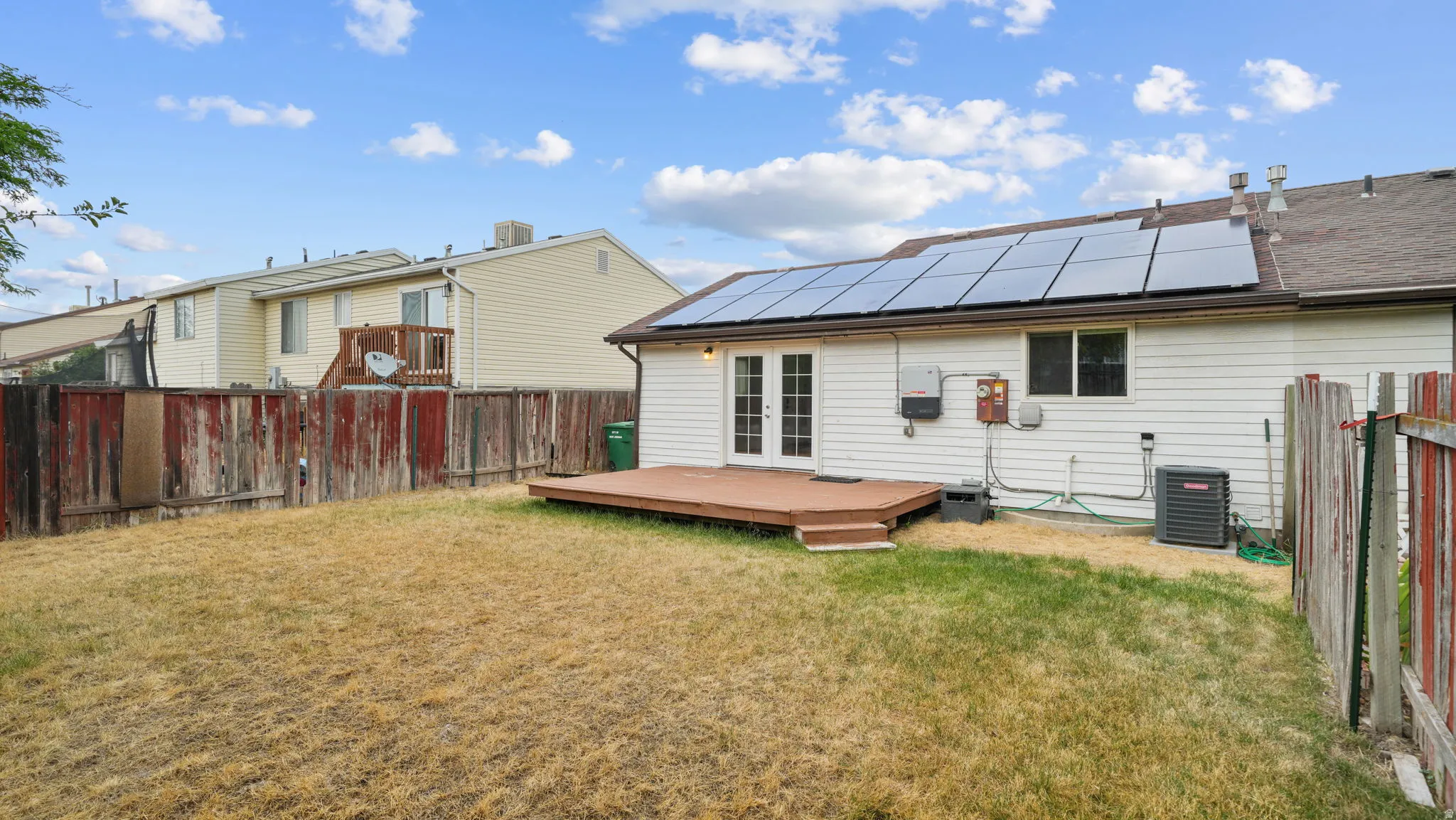 Rear exterior featuring a wood deck, solar panels and fencing.