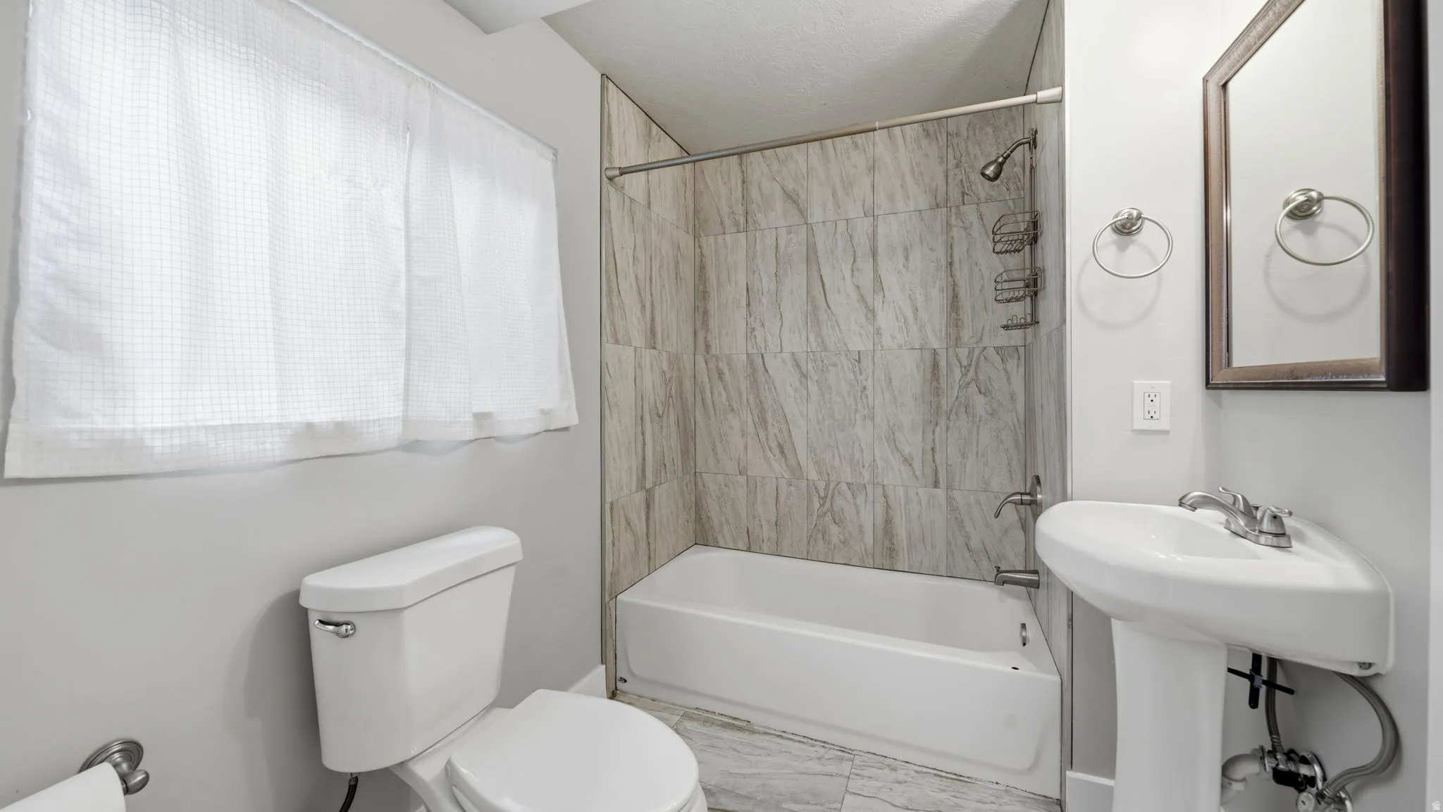 Full bathroom featuring a pedestal sink, framed mirror, and full-height surround tile