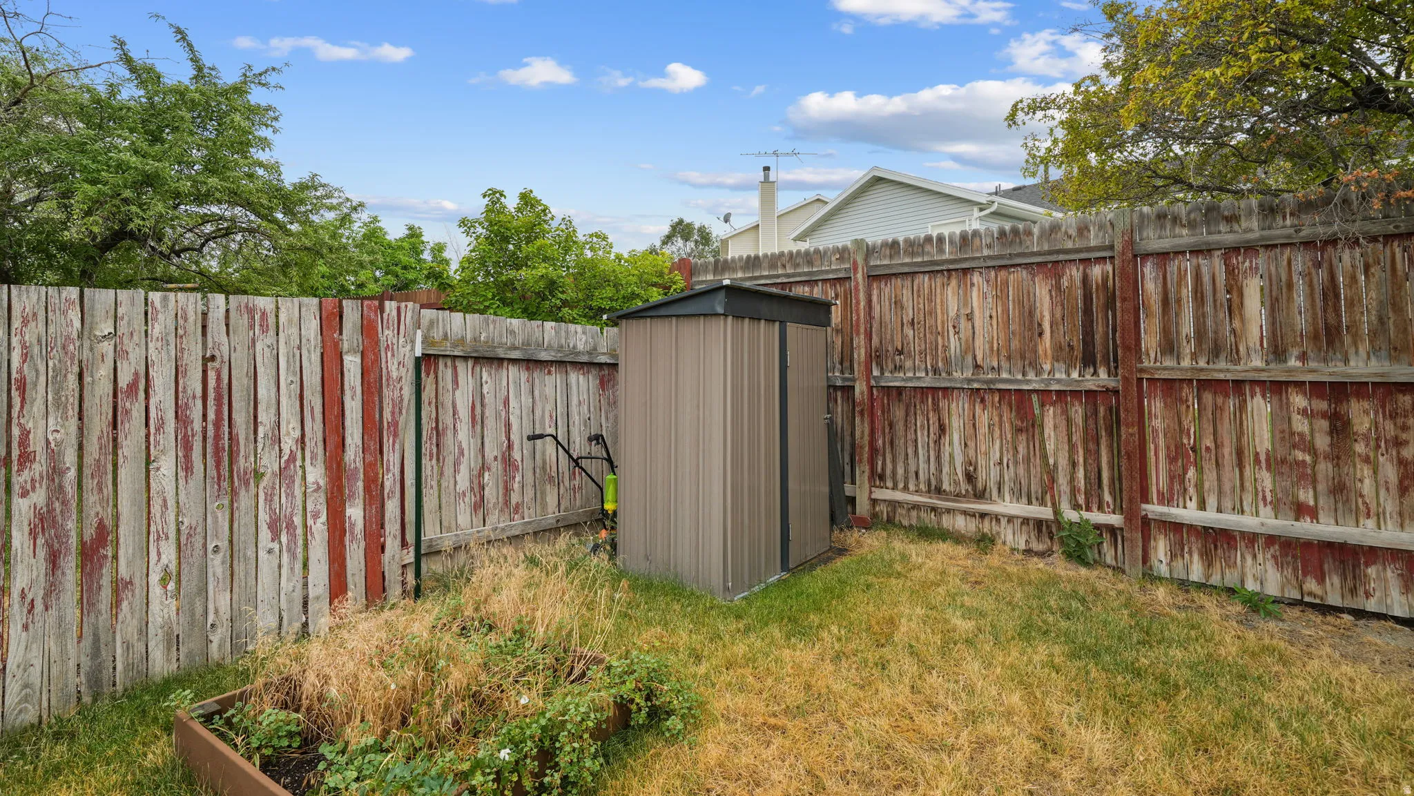 Outdoor storage shed in west corner of backyard and a garden bed.