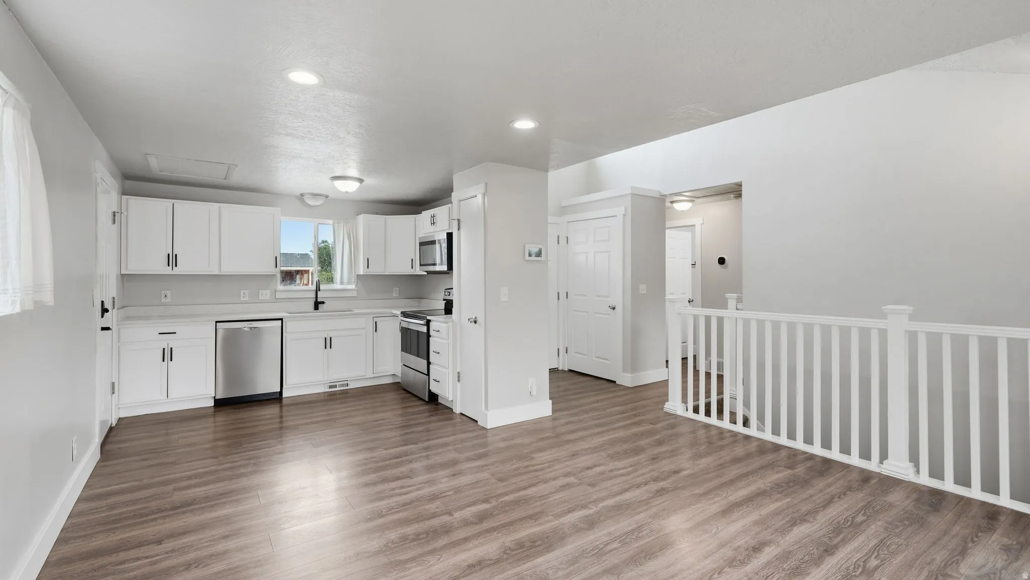 Open-concept kitchen, pantry and living area featuring wood-finish flooring, white cabinetry, and stainless steel appliances
