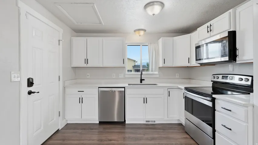 Kitchen with pantry closet featuring quartz countertops, large sink, stainless steel appliances, a view of the Wasatch mountains, and a side door to the yard.