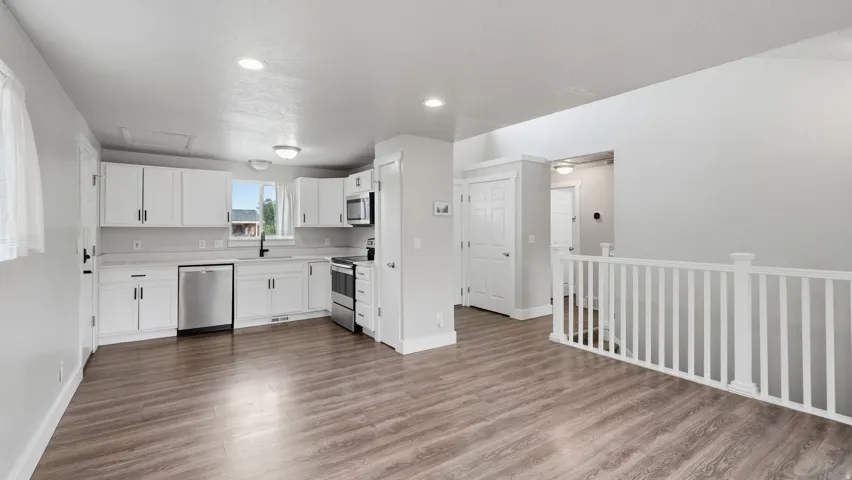 Open-concept kitchen, pantry and living area featuring wood-finish flooring, white cabinetry, and stainless steel appliances