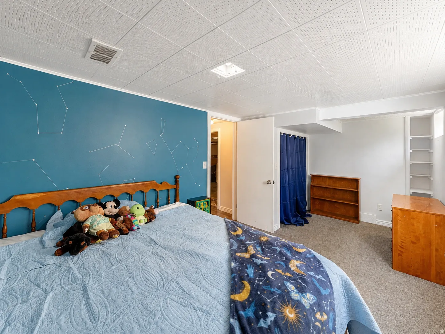 Carpeted bedroom featuring a patterned accent wall, white drop ceiling with recessed lighting, and a built-in shelving unit