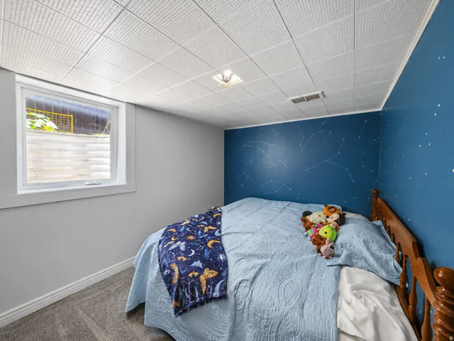 Room featuring a drop ceiling with recessed lighting, blue accent wall with constellation motif, gray carpeting, and a white-framed window