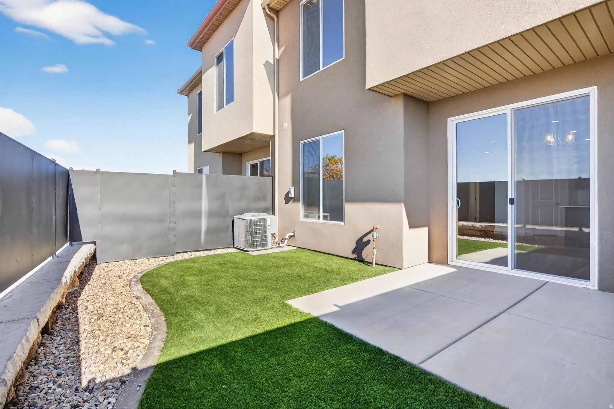 Private patio area featuring a concrete slab, artificial turf, and decorative rock landscaping