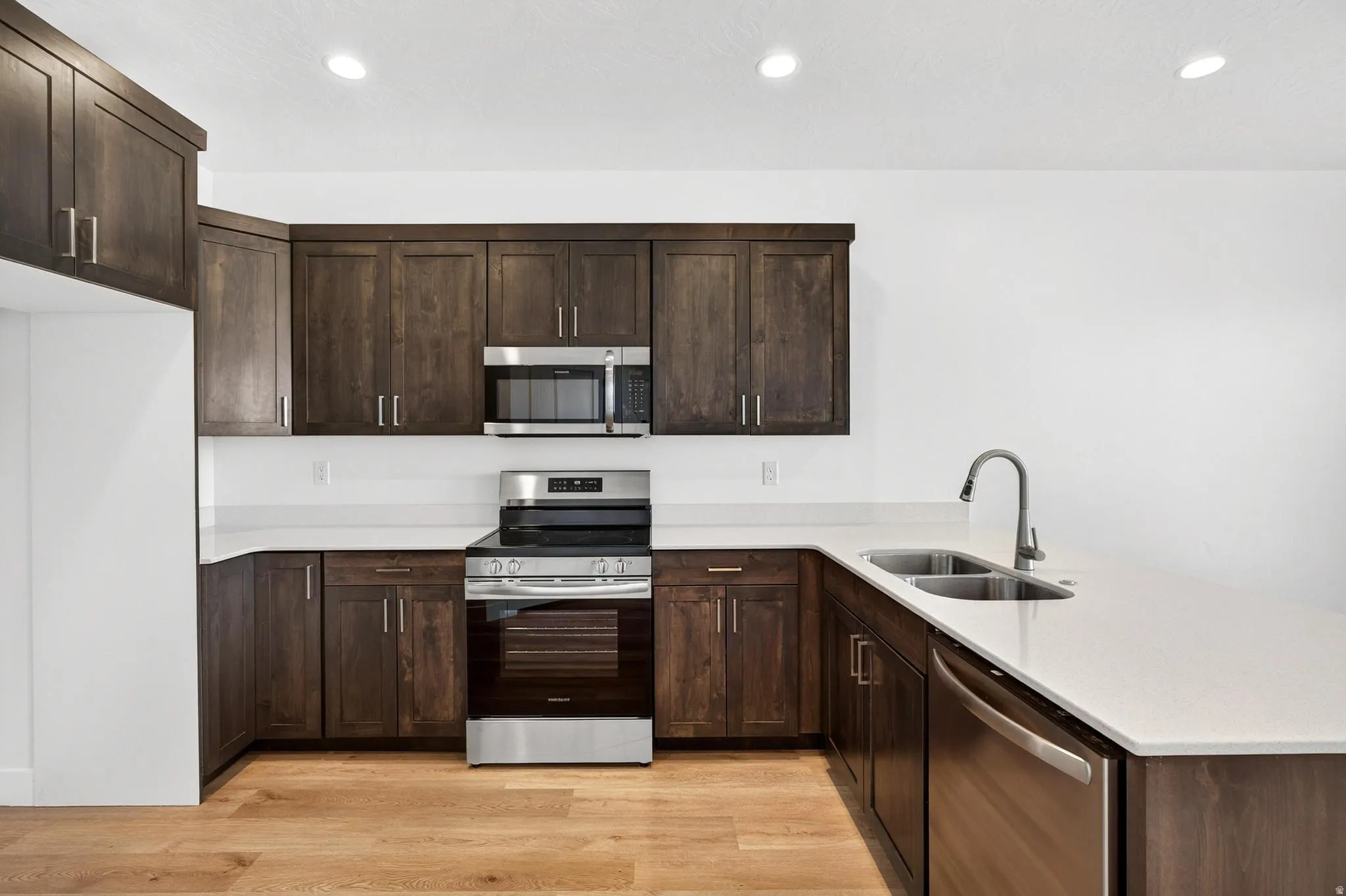 Kitchen featuring dark wood cabinetry, light-toned countertops, and stainless steel appliances including a range, microwave, and dishwasher