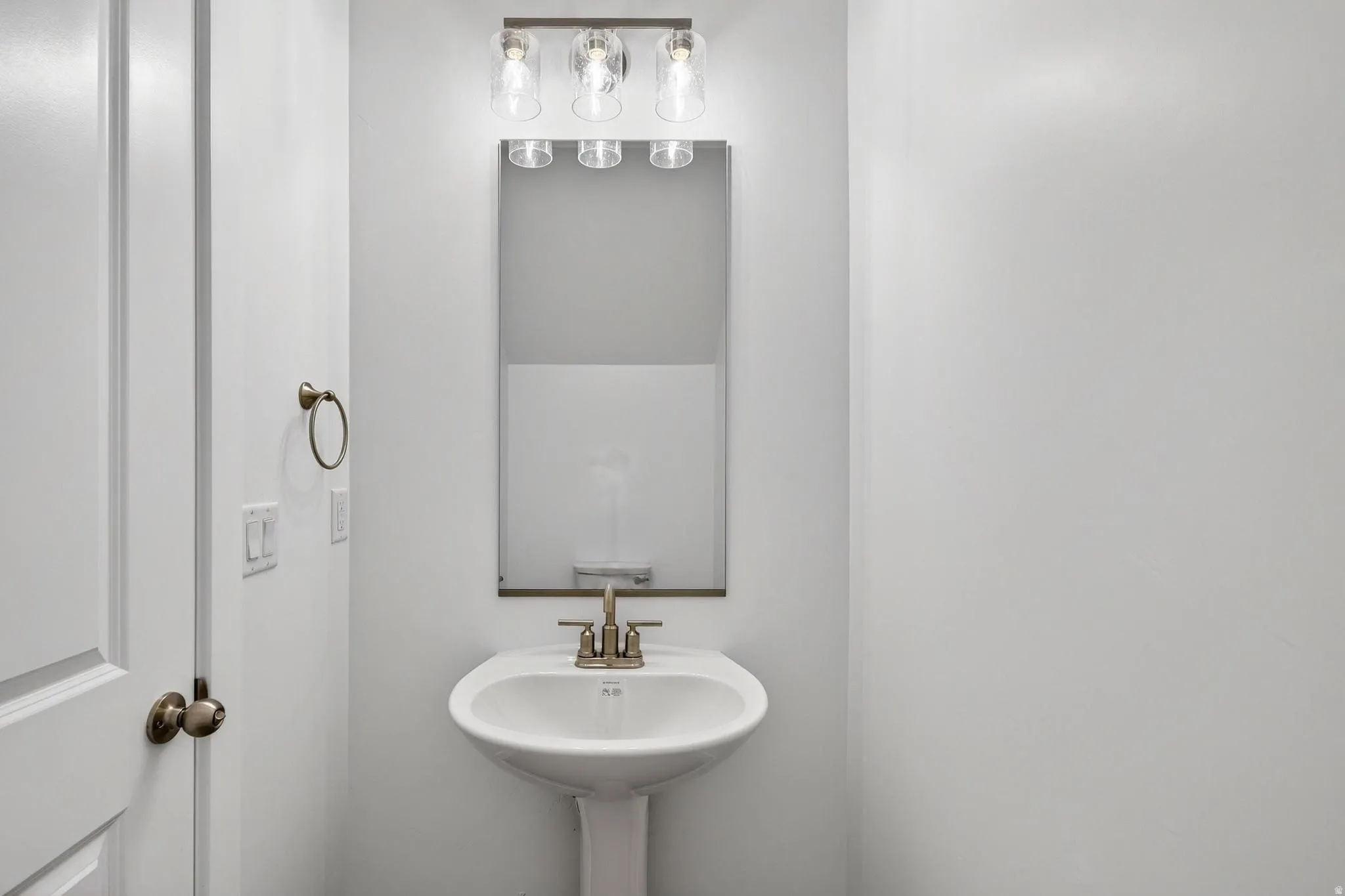 Pedestal sink with brushed nickel faucet, framed by a rectangular mirror and a three-light vanity fixture