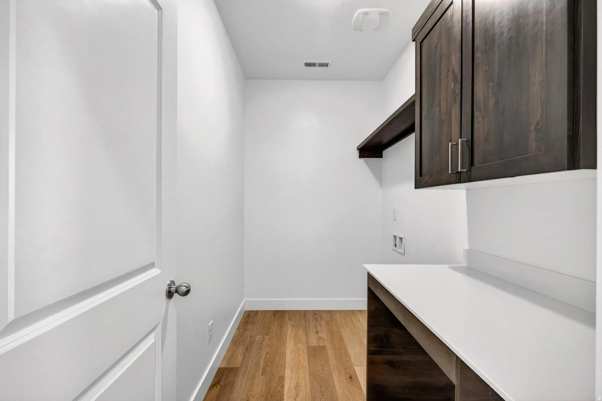 Laundry area featuring wood-finish flooring, dark wood cabinetry with brushed nickel hardware, a built-in shelf, and a white countertop