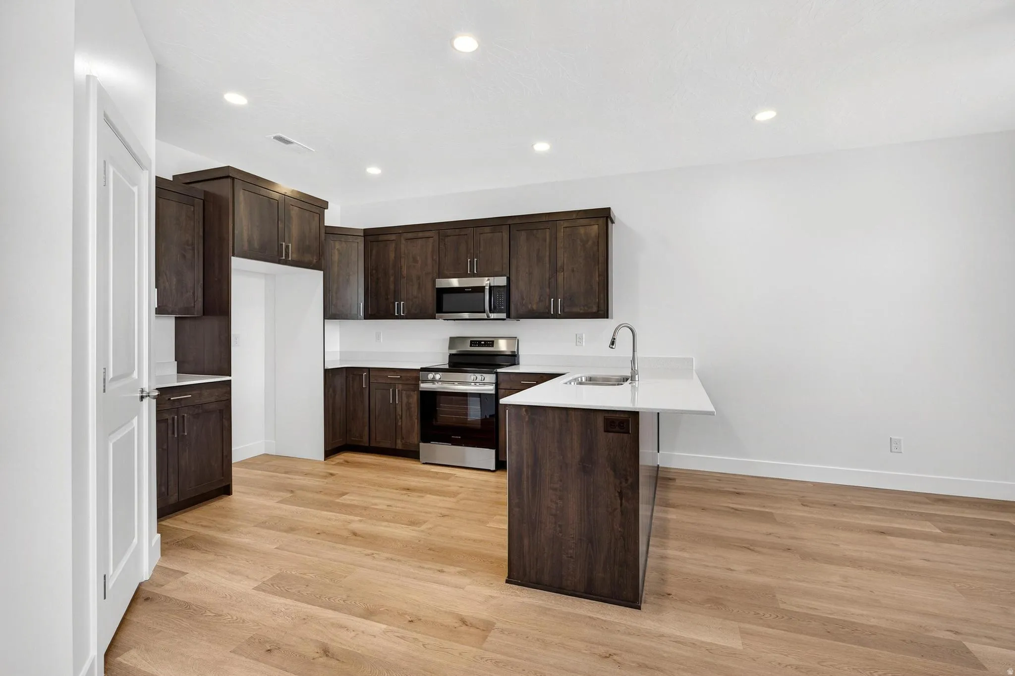 Kitchen featuring wood-finish flooring, dark wood cabinetry, a white countertop island with an undermount sink, and stainless steel appliances