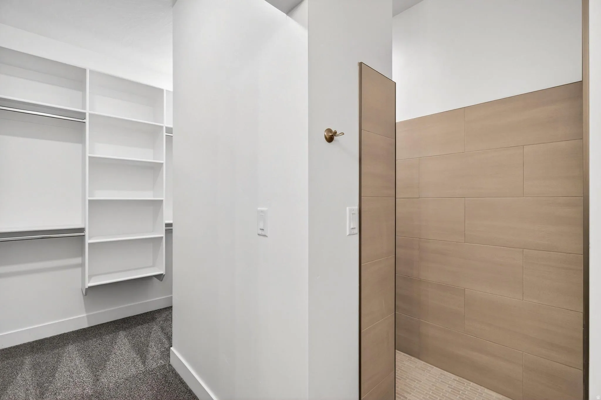 Walk-in closet with custom shelving and hanging rods, accompanied by an open shower featuring large-format wall tiles and a textured floor
