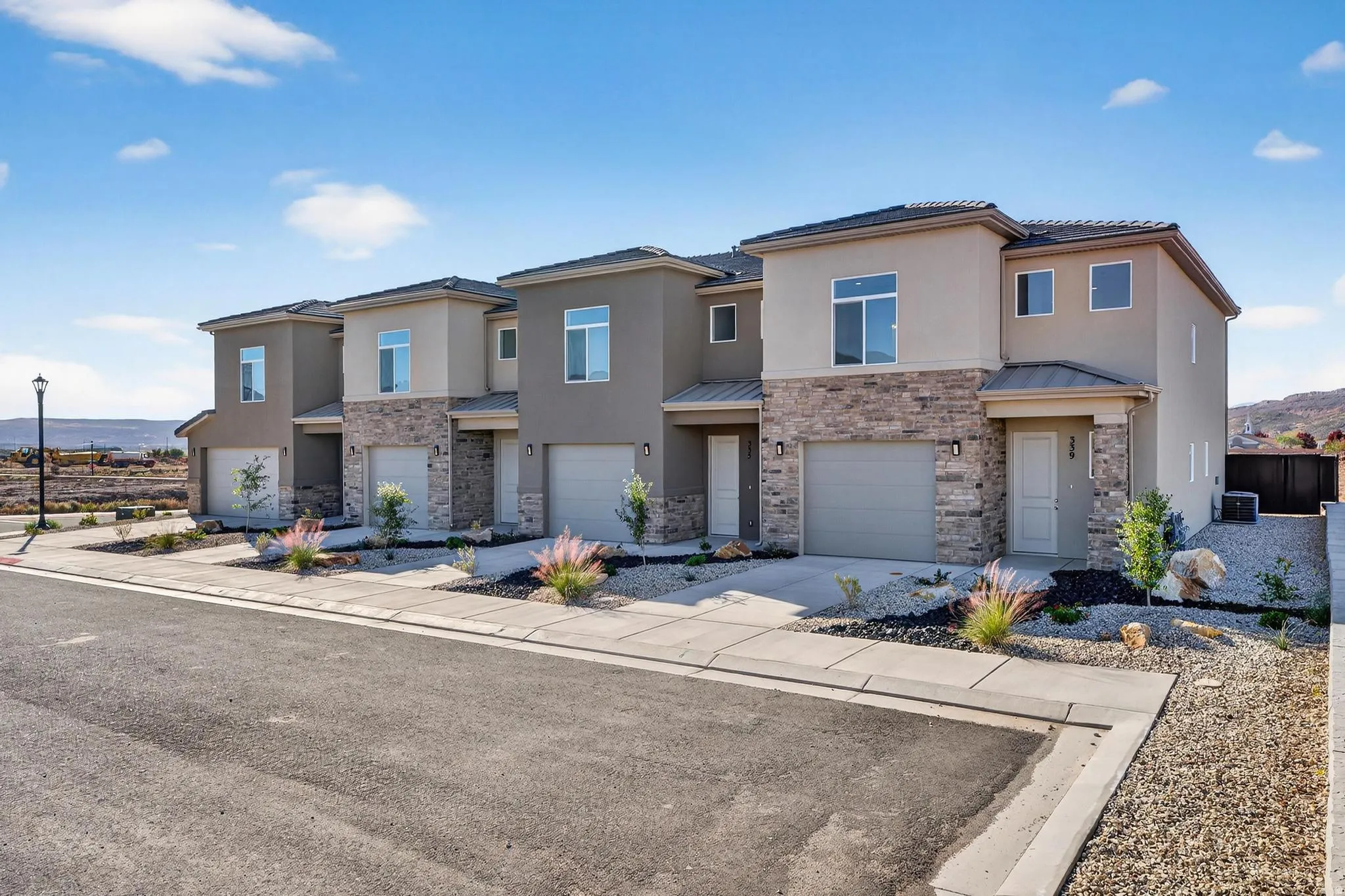 Contemporary townhome exterior featuring a stucco and stone facade, private garage, and desert-inspired landscaping