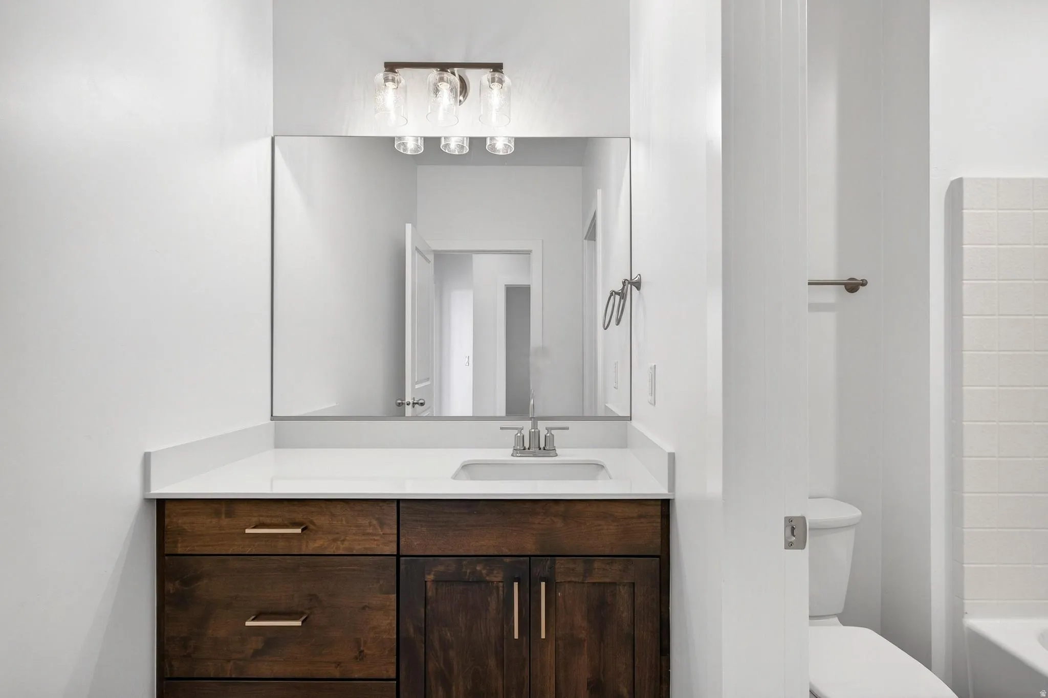 Bathroom vanity featuring a dark wood-finish cabinet with brass hardware, a white countertop, and an undermount sink with a chrome faucet