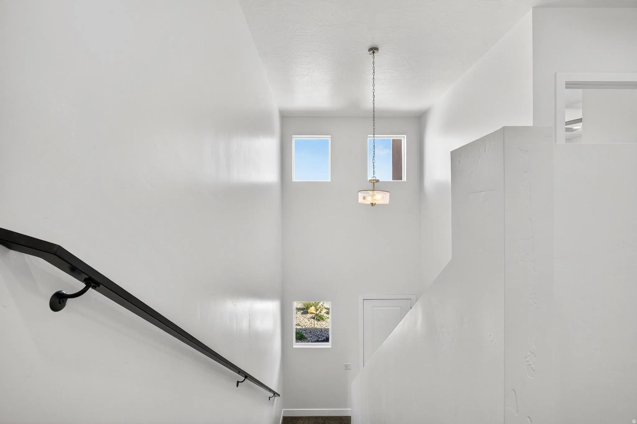 Two-story foyer with high ceilings, multiple square windows, and a black handrail