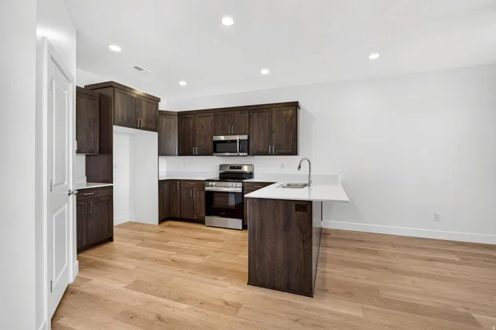 Kitchen featuring wood-finish flooring, dark wood cabinetry, a white countertop island with an undermount sink, and stainless steel appliances