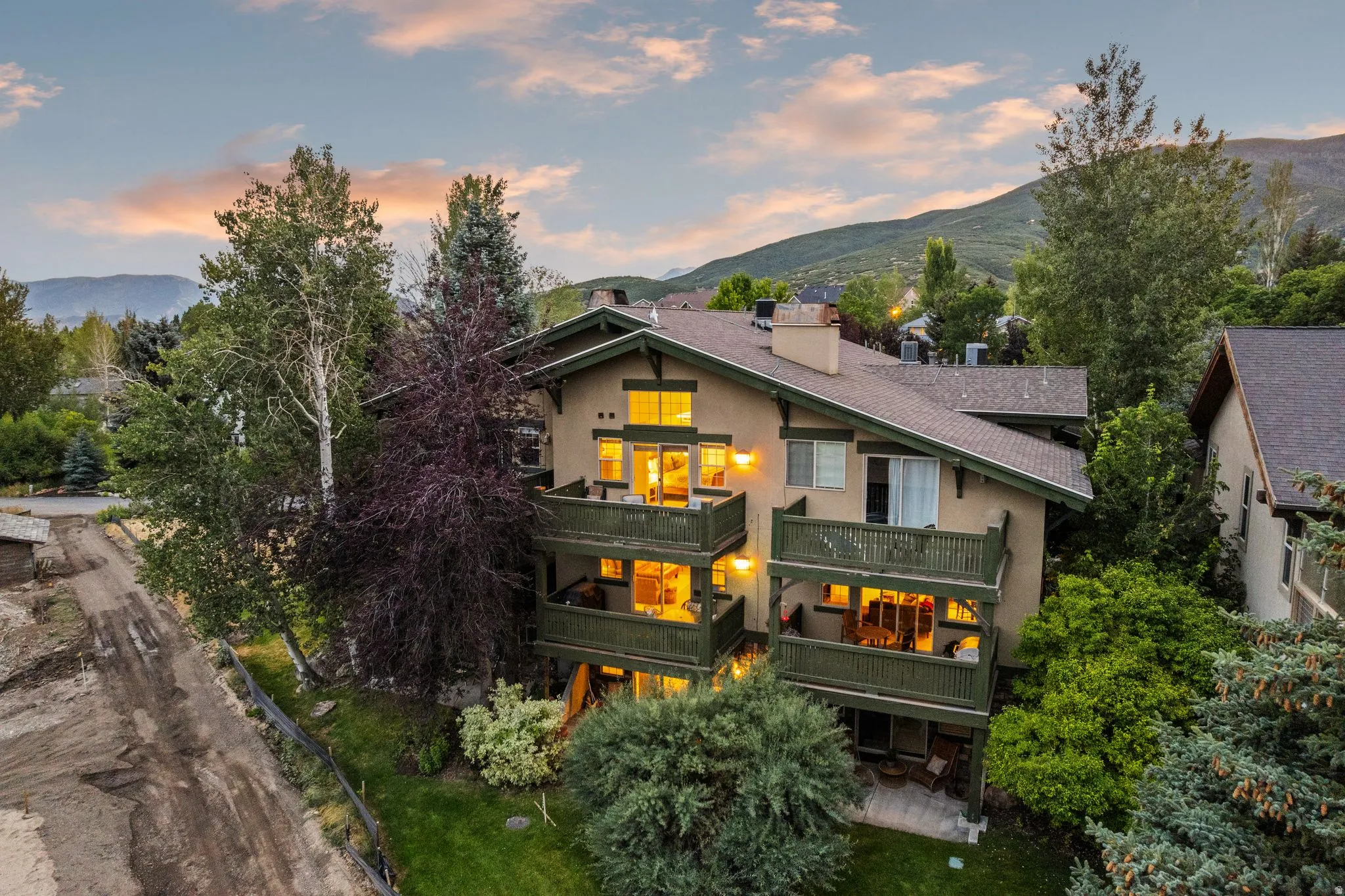 Multi-level residence featuring balconies with dark green railings, a stucco exterior, and a sloped roofline