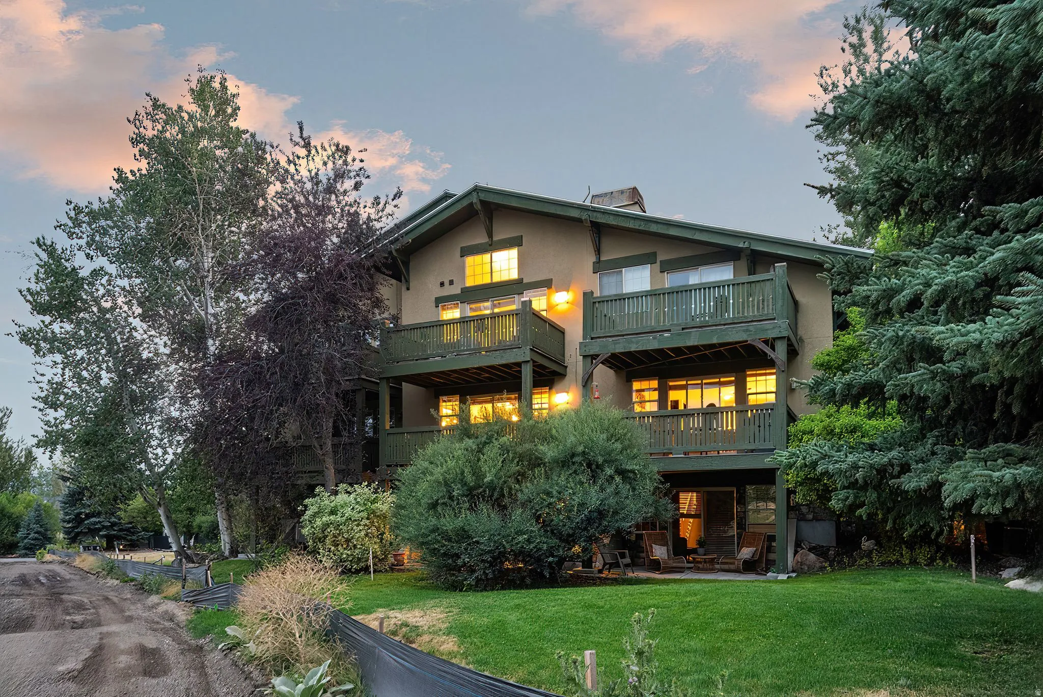 Multi-level stucco exterior with two balconies, a ground-level patio, and surrounding mature trees