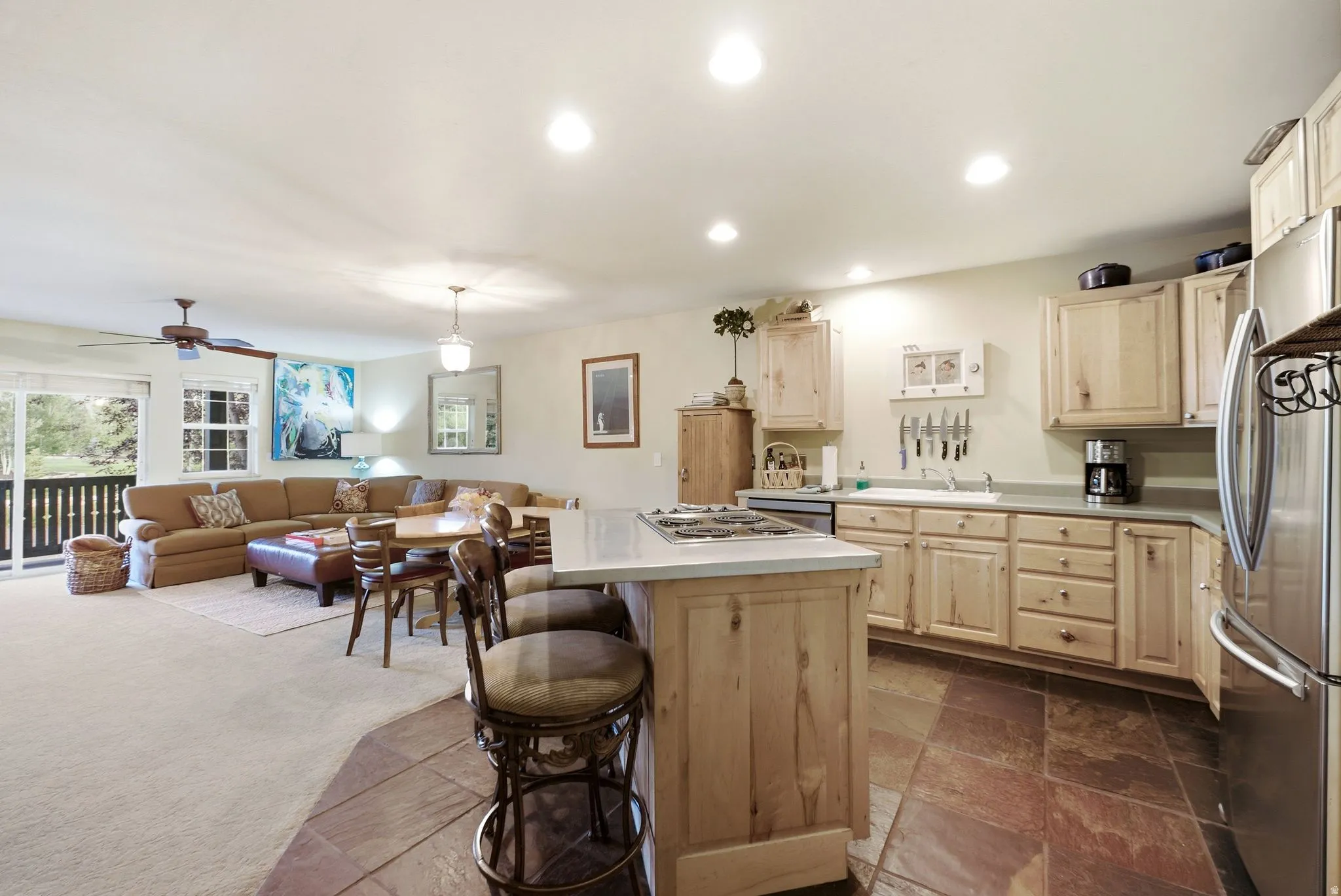 Open-concept kitchen featuring light wood cabinetry, a central island with a cooktop, and stainless steel appliances