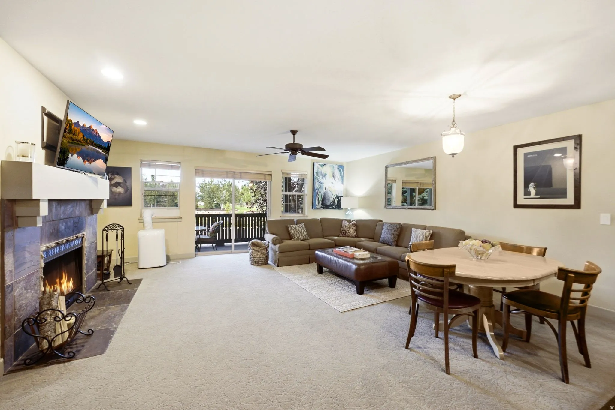 Spacious living area featuring a stone-faced fireplace with a white mantel, recessed lighting, and access to an outdoor balcony