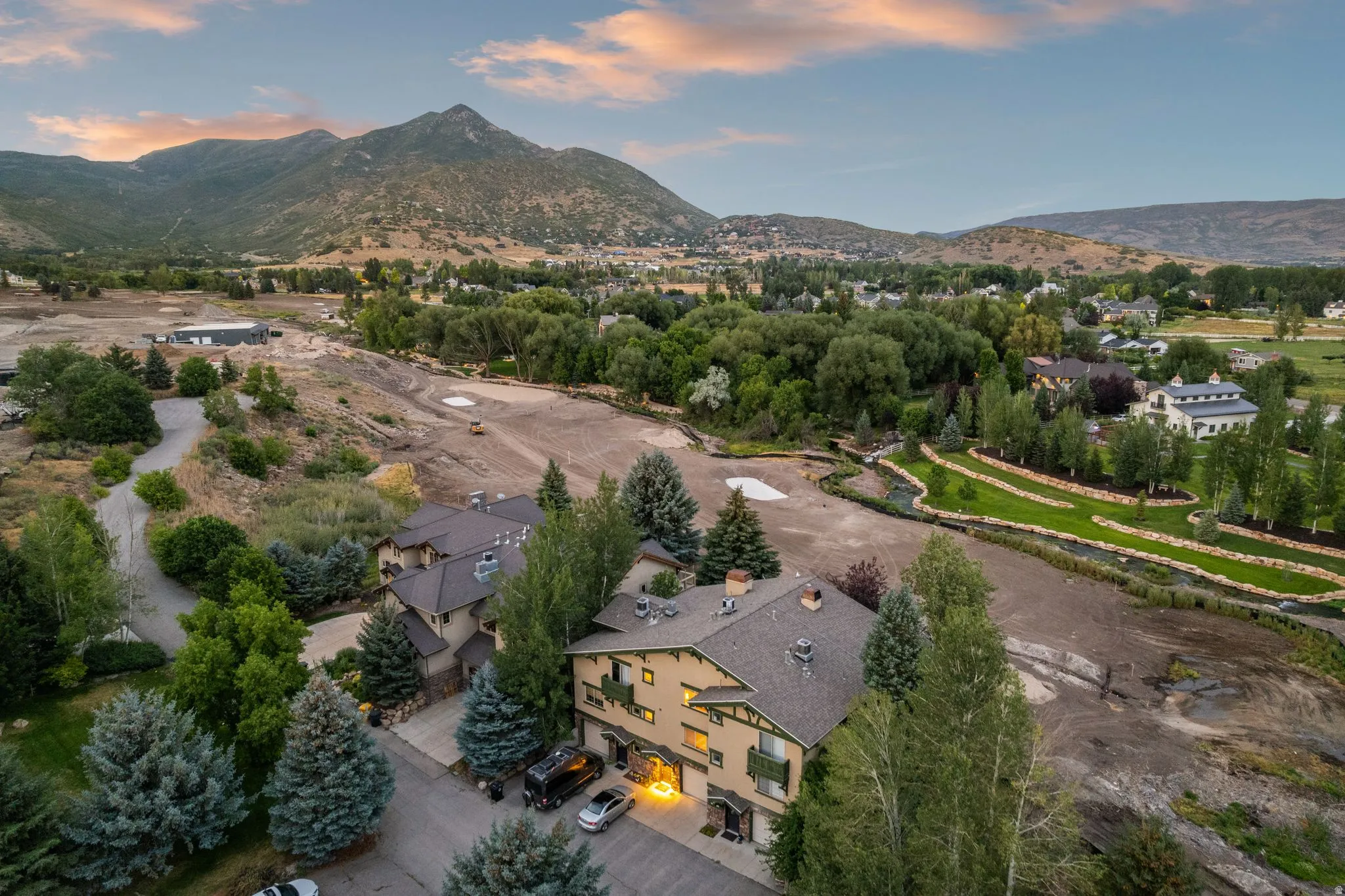 Aerial perspective showcasing multiple residential structures, surrounded by varied mature trees, with a prominent mountain range backdrop