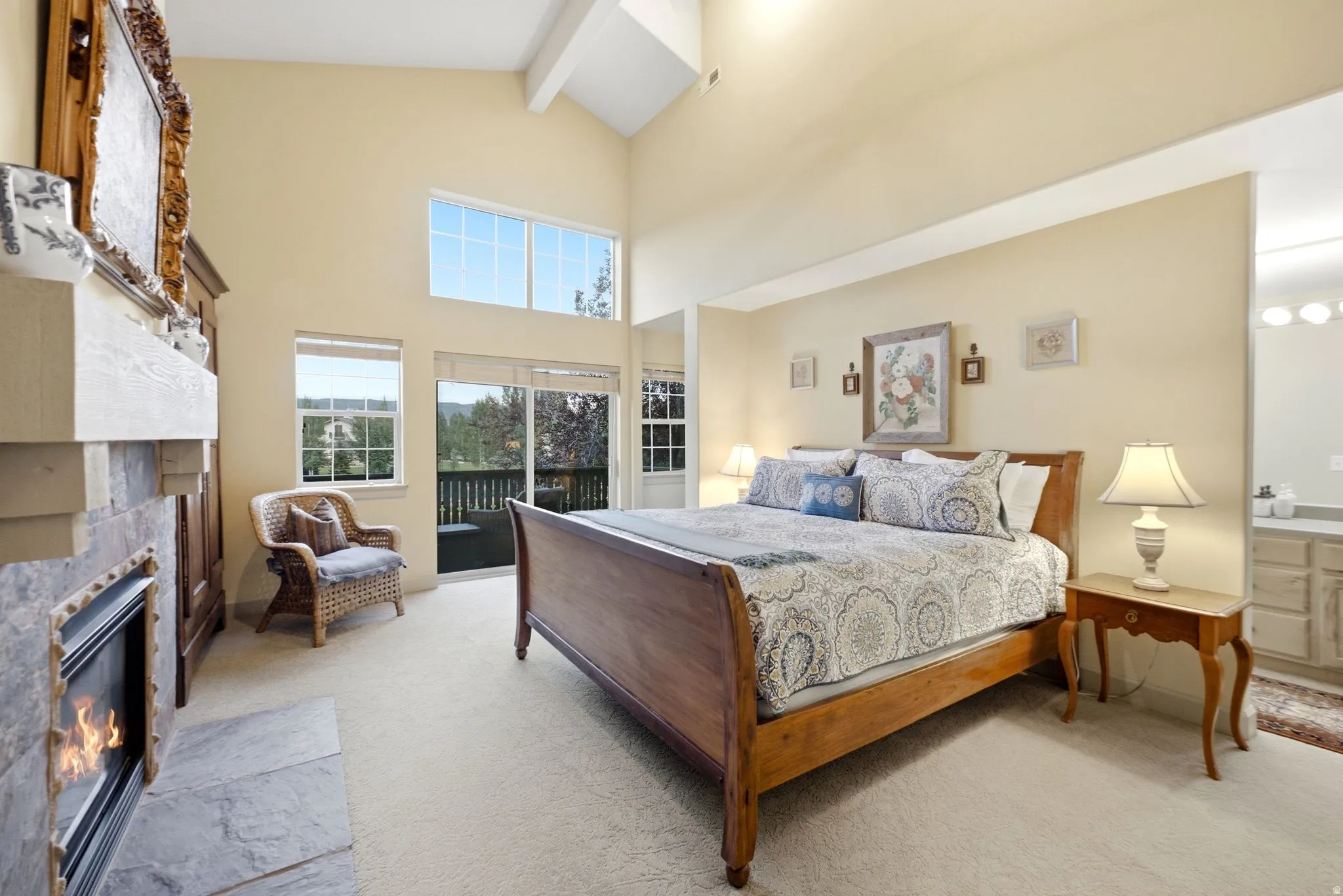 Spacious room featuring vaulted ceilings, a stone-clad fireplace with a hearth, carpeted flooring, and a sliding glass door opening to an outdoor deck