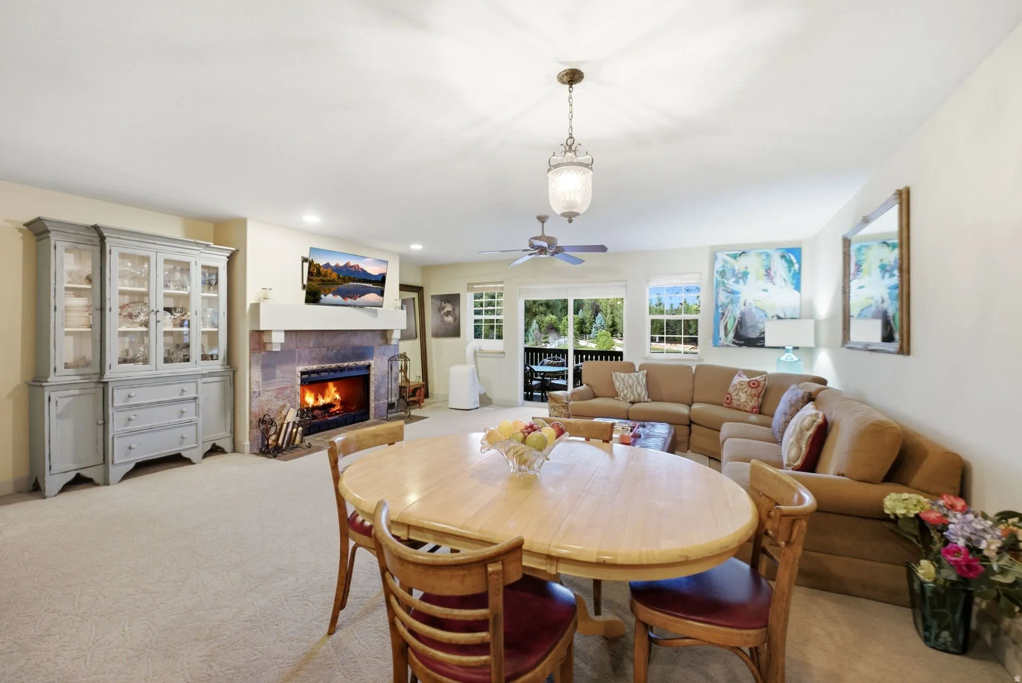 Open-concept living space with a stone-surround fireplace, light-toned carpet flooring, and a sliding glass door providing exterior access