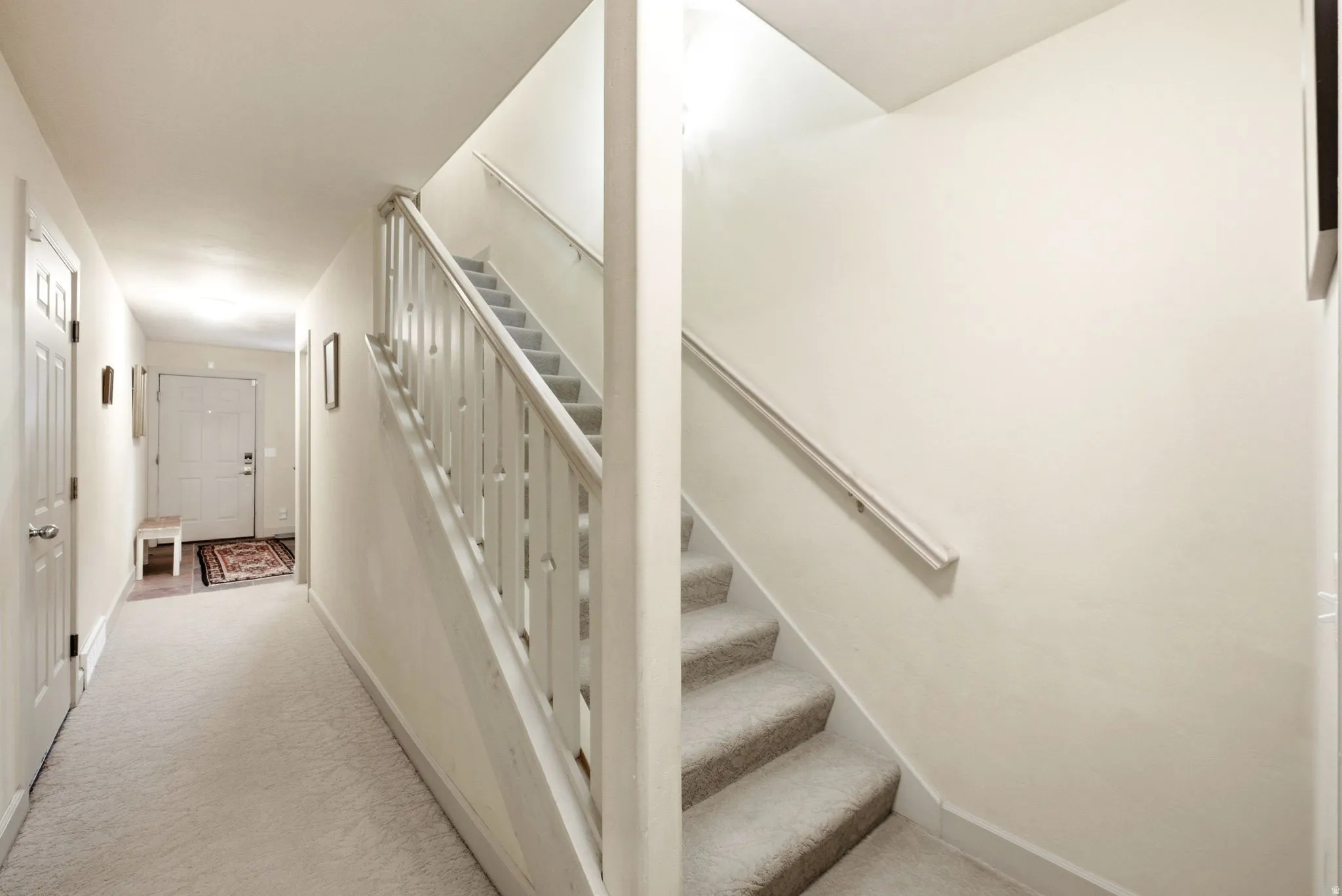 Carpeted staircase with white balusters and handrail, featuring recessed lighting, a white entry door, and light-colored walls