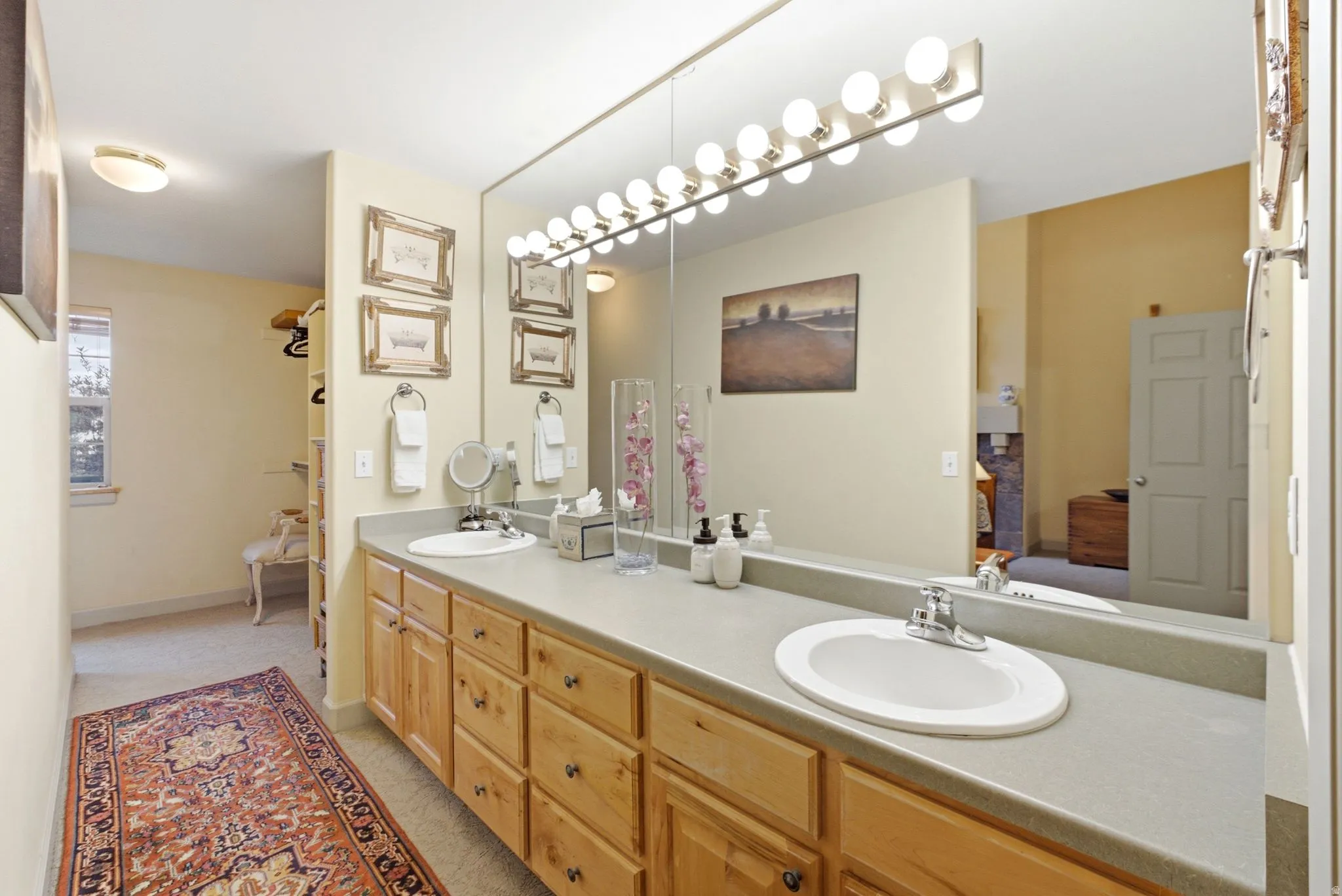 Double vanity featuring wood cabinetry, integrated sinks, and a large wall-mounted mirror with overhead lighting