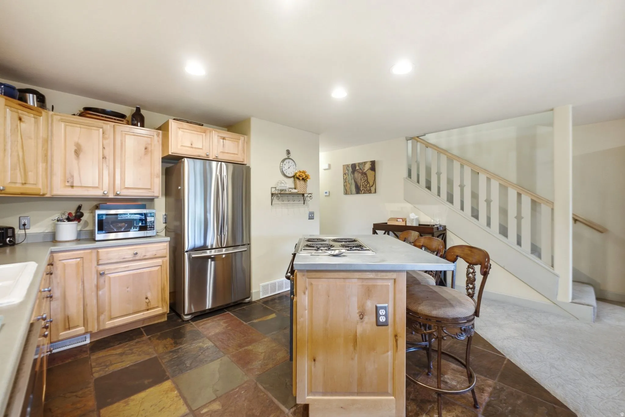 Kitchen featuring natural wood cabinetry, stainless steel refrigerator, dark tiled flooring, recessed lighting, and a kitchen island with cooktop